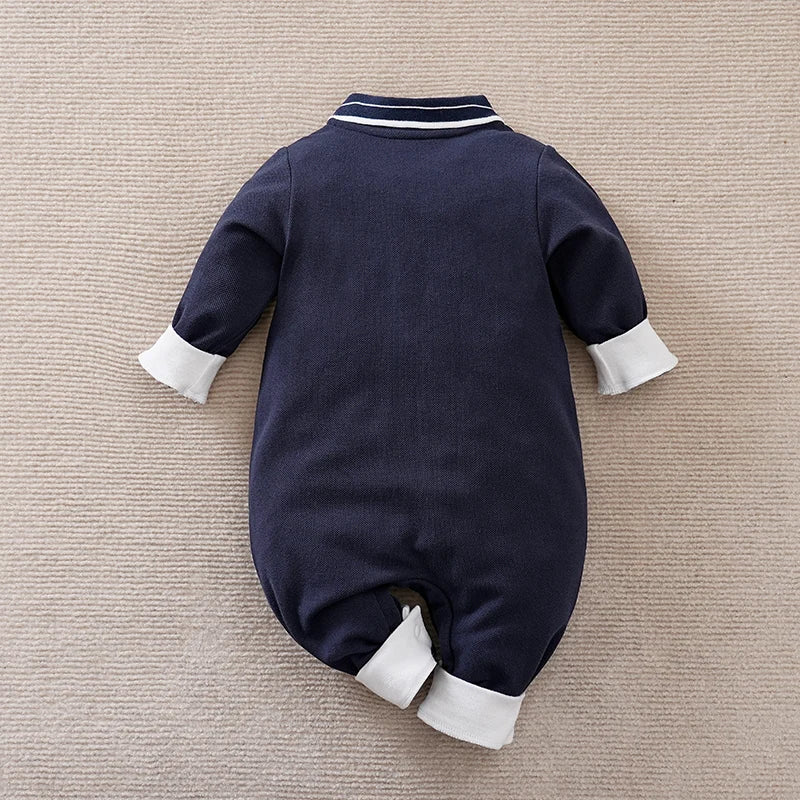 Navy baby romper with white cuffs and trim on a beige surface