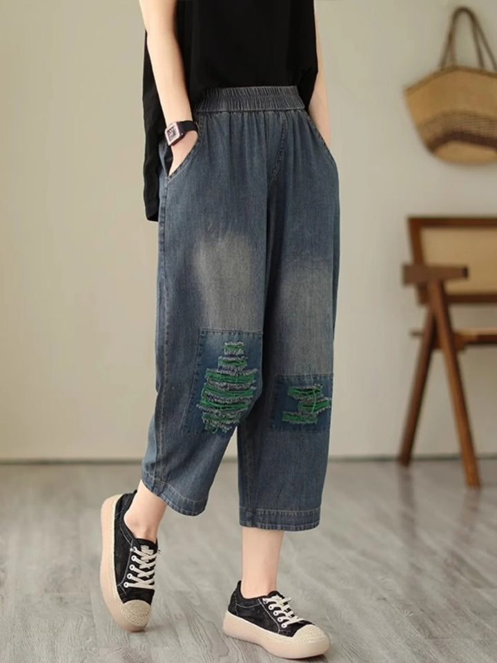 Person wearing blue denim capri pants with patches in a room.