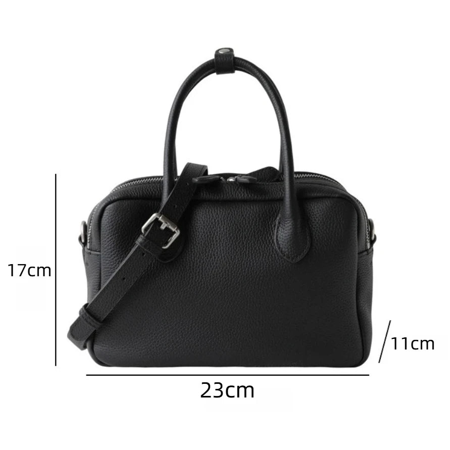 Black pebbled leather handbag with two top handles and a detachable shoulder strap, shown with dimension lines and measurements: 17 cm height, 23 cm width, and 11 cm depth on a white background.