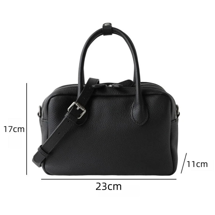 Black pebbled leather handbag with two top handles and a detachable shoulder strap, shown with dimension lines and measurements: 17 cm height, 23 cm width, and 11 cm depth on a white background.