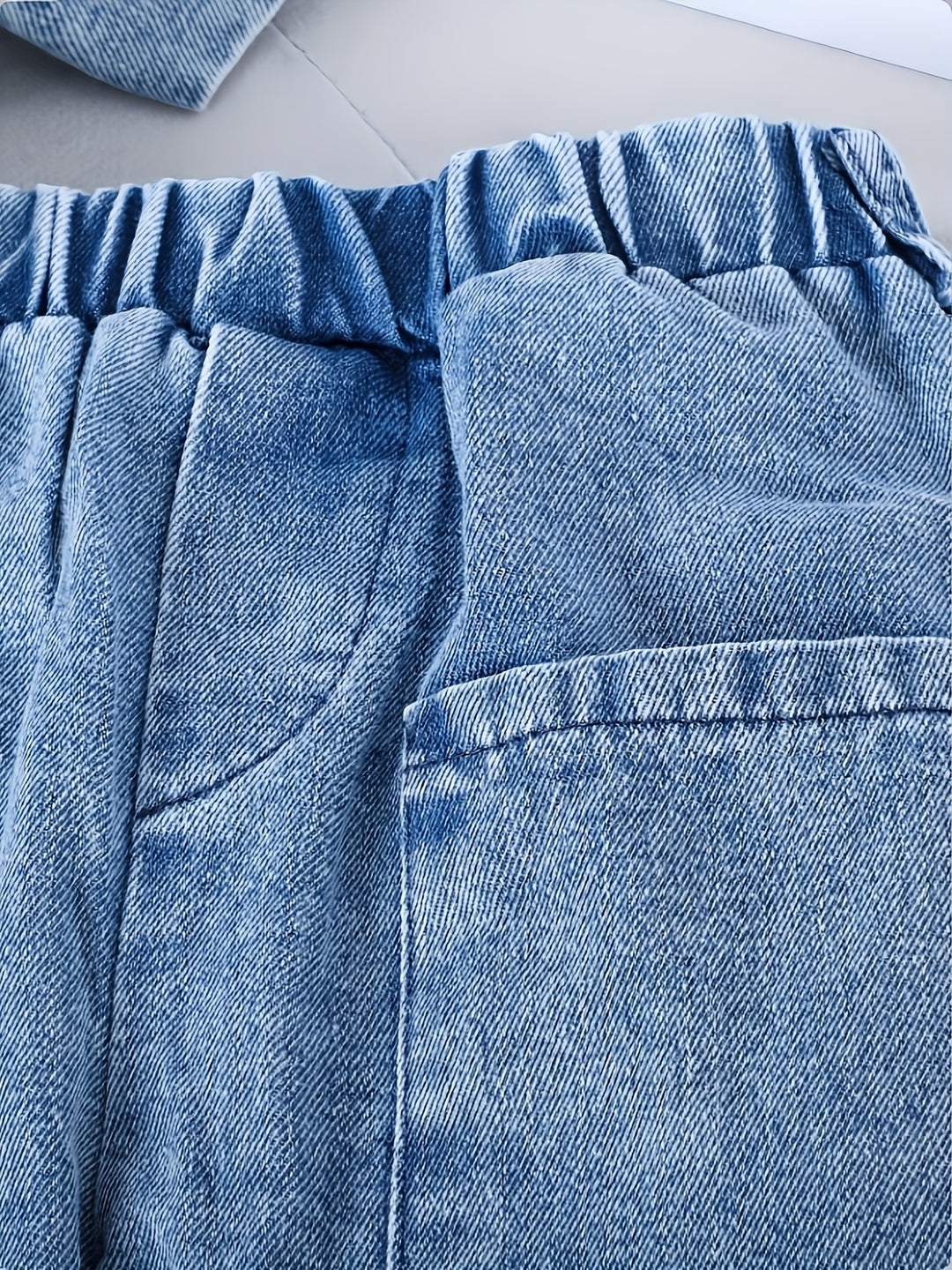 Close-up of blue denim pants with a pocket detail on a light background