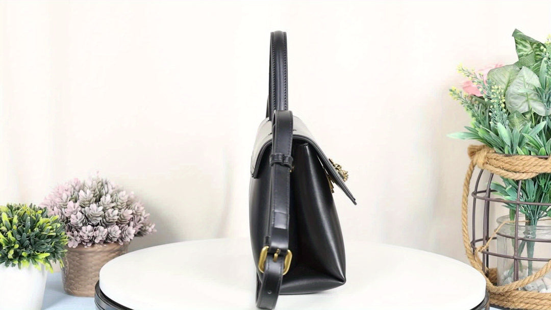 Black handbag on a white surface with decorative plants in the background