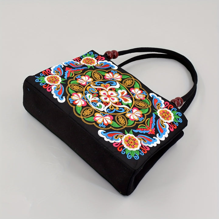 Black handbag with colorful floral embroidery on a light gray background