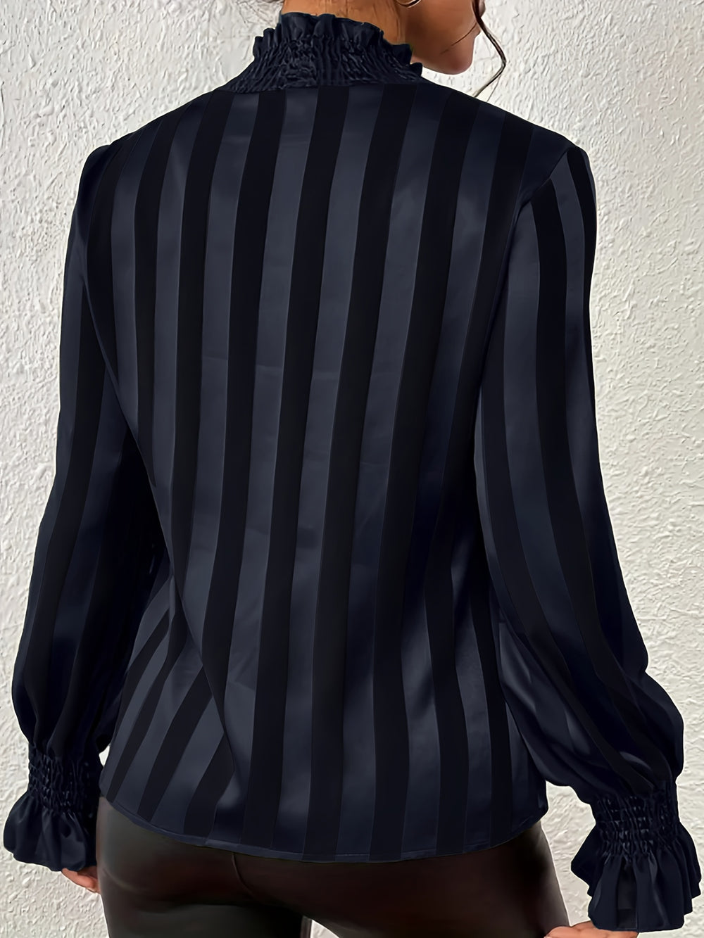 Black and gray striped blouse worn by a person against a white wall