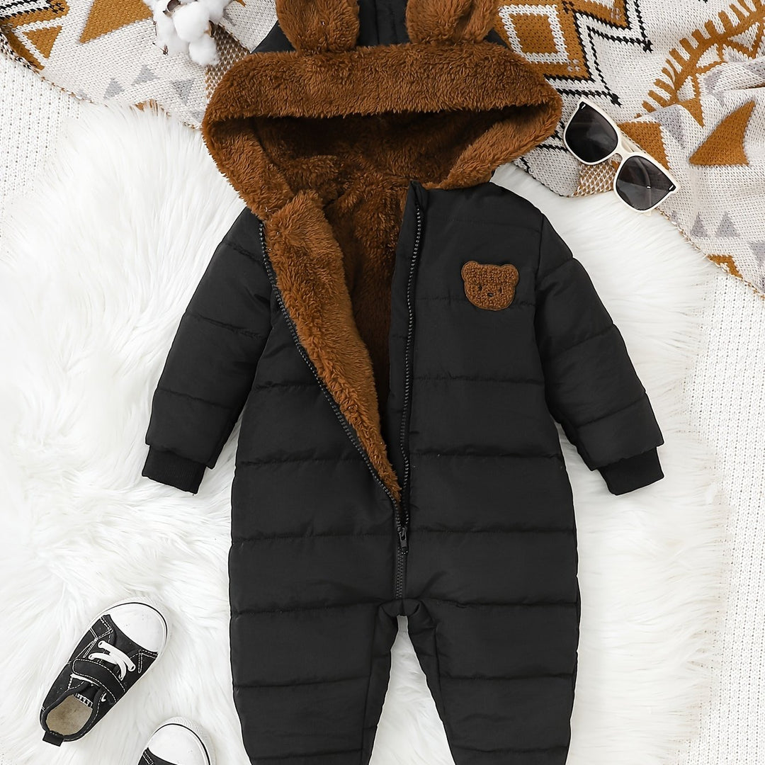Black puffer snowsuit with brown fur hood on a white surface, surrounded by accessories.