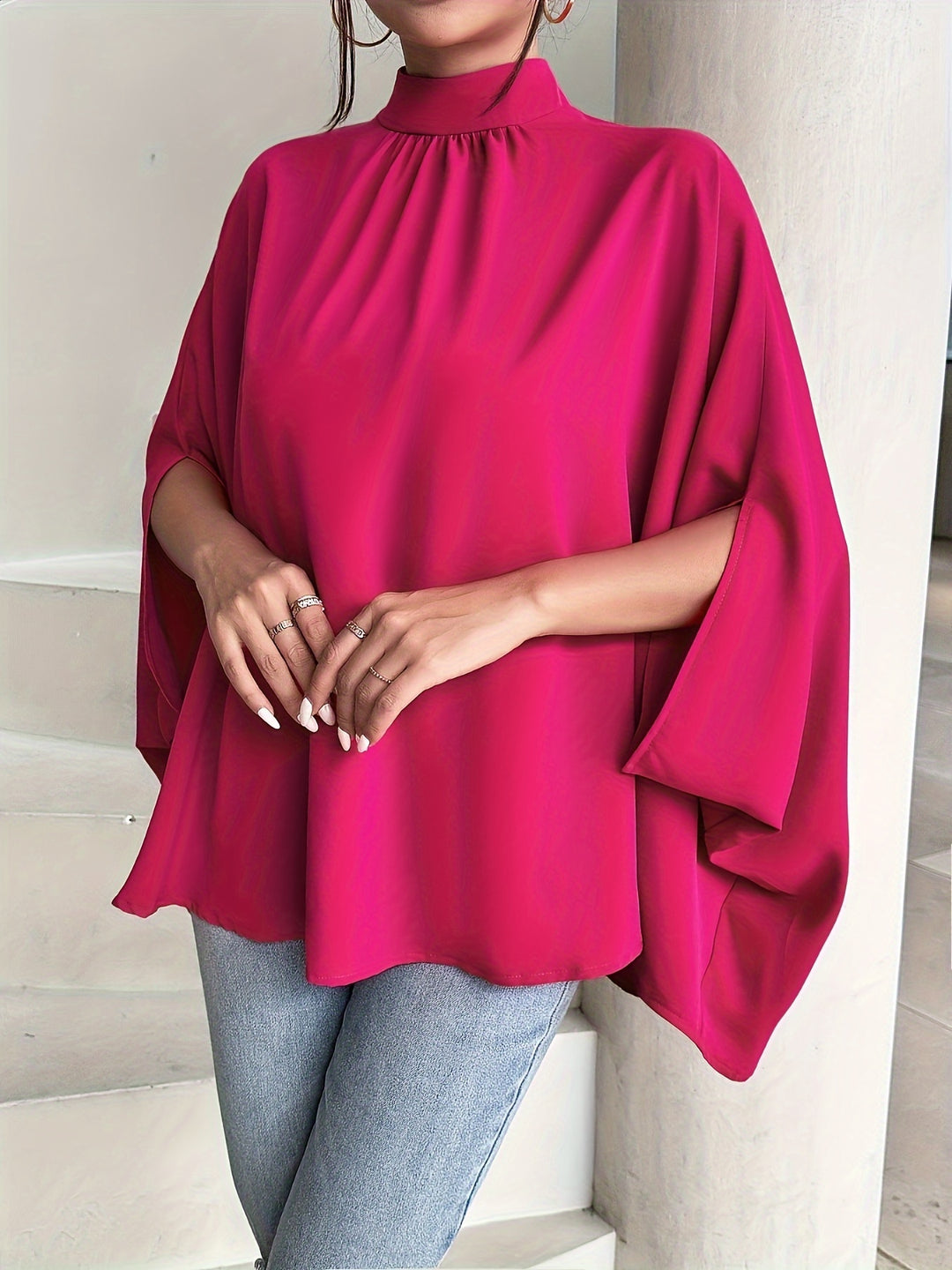 Person wearing a bright pink poncho over a light blue outfit indoors.