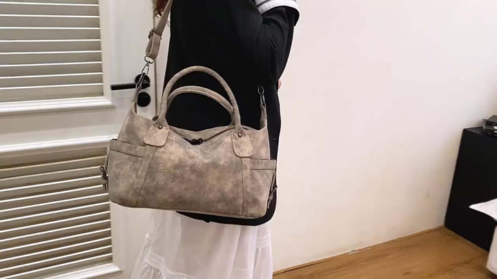 Person holding a gray handbag indoors with a neutral background