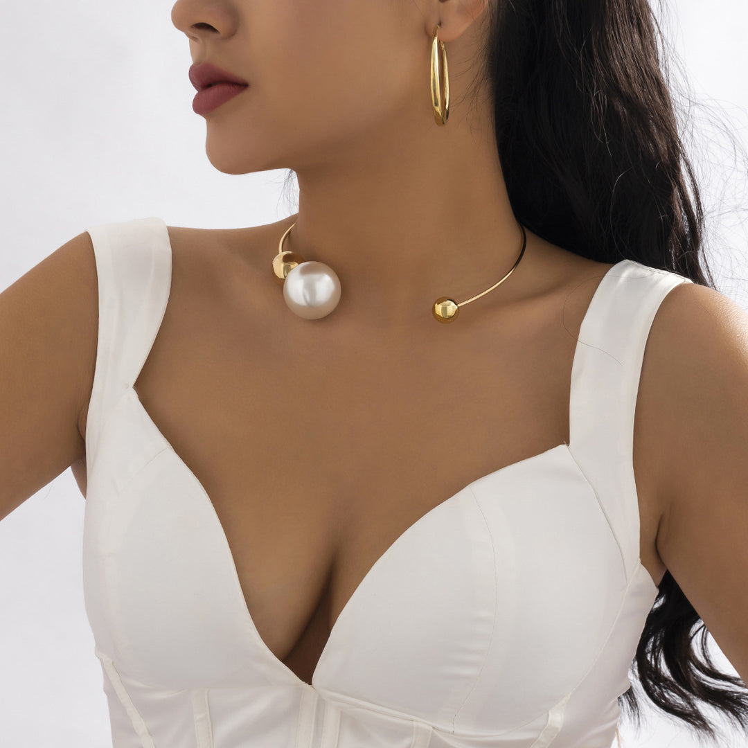 Woman wearing a white top with gold jewelry including earrings and a necklace on a plain background