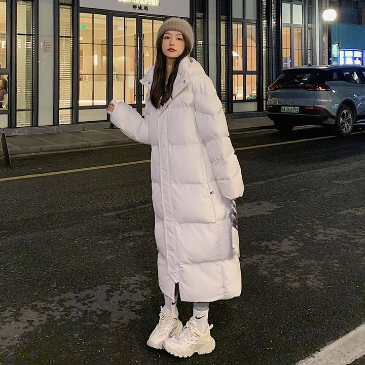 Women's White Longline Padded Winter Coat Styled With A Knit Hat And White Sneakers.