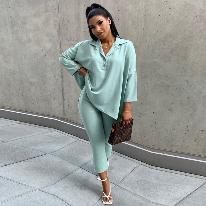 Woman in a light green outfit standing against a concrete wall.