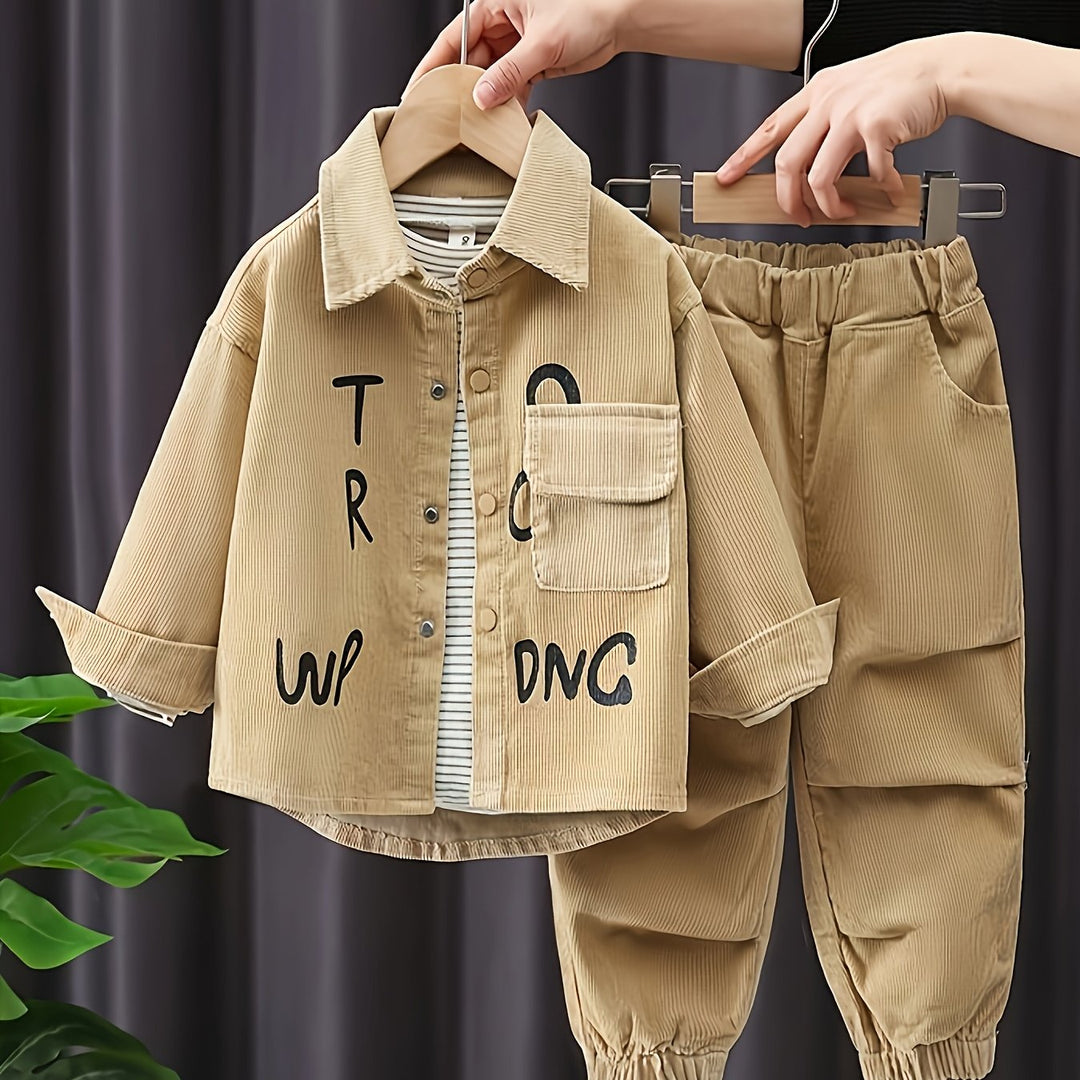 Beige children's jacket and pants with text on a hanger against a dark curtain background.