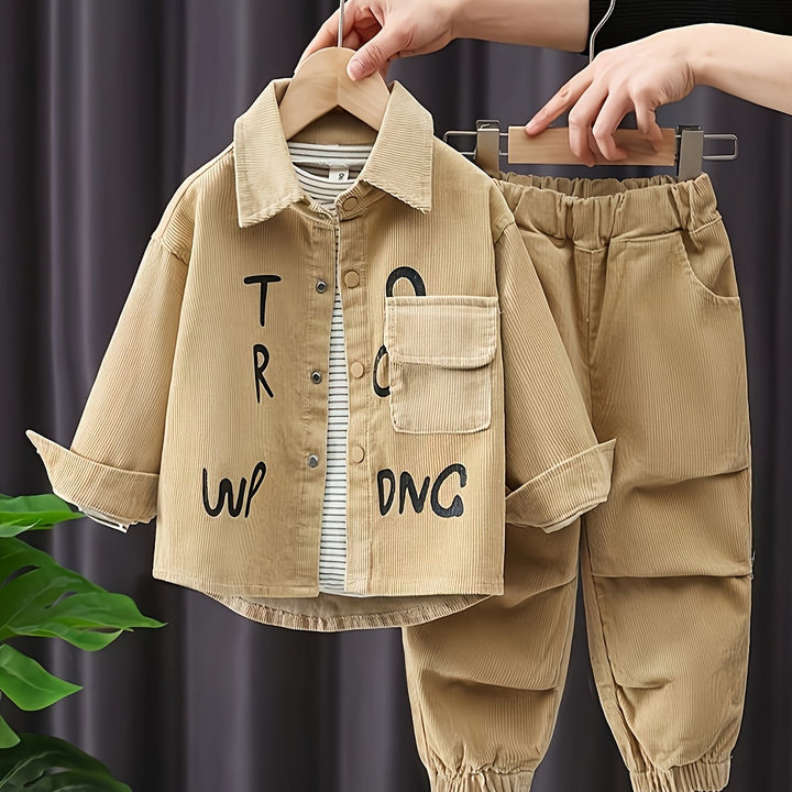 Beige children's jacket and pants with text on a hanger against a dark curtain background.