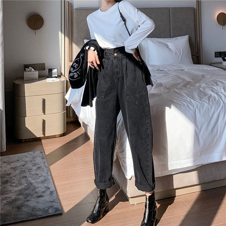 Person wearing a white shirt, black jacket, and dark jeans in a bedroom.