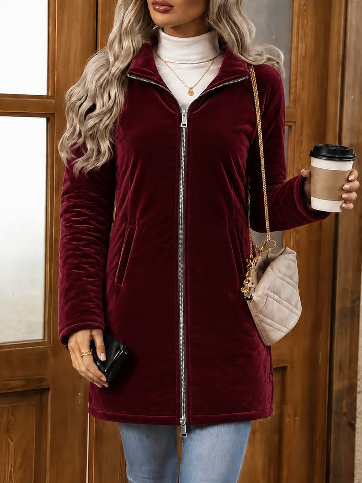 Women's Wine Red Velvet Long Coat With Mock Neck And Two-Way Zipper, Styled With Light Blue Jeans.