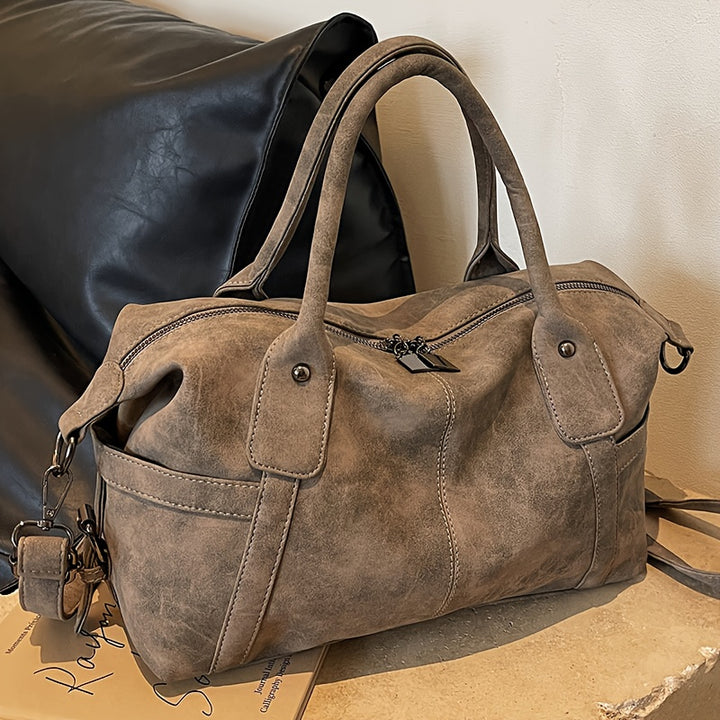 Brown leather duffel bag on a textured surface with a neutral background