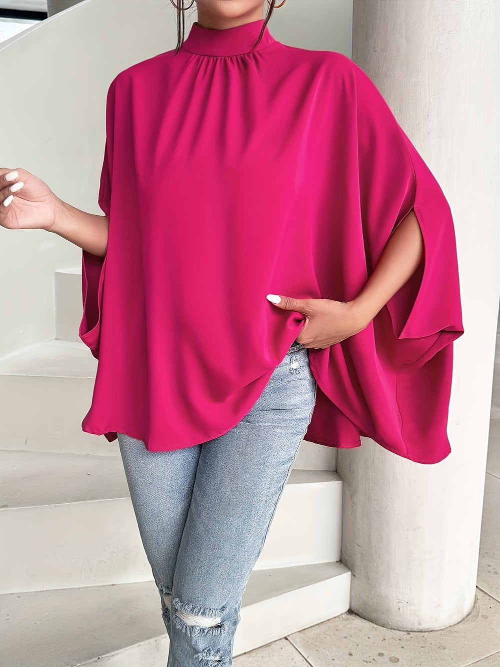 Person wearing a bright pink poncho over a light blue outfit on a neutral background