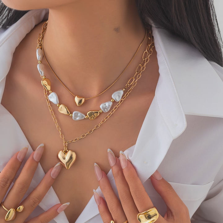 video of a Gold heart-shaped necklace with white stones on a model wearing a white top.
