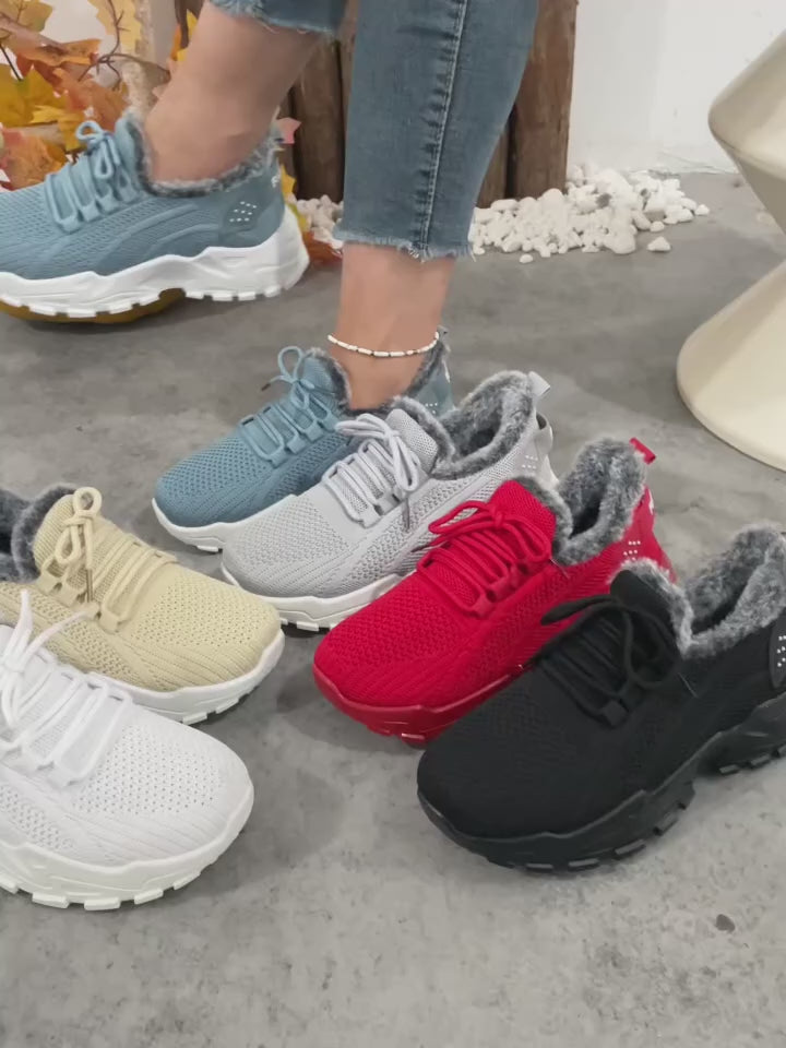 Video of knitted slip-on sneakers with white soles and gray faux-fur lining, shown with one shoe being held by a hand and the other worn on a foot with a bracelet.