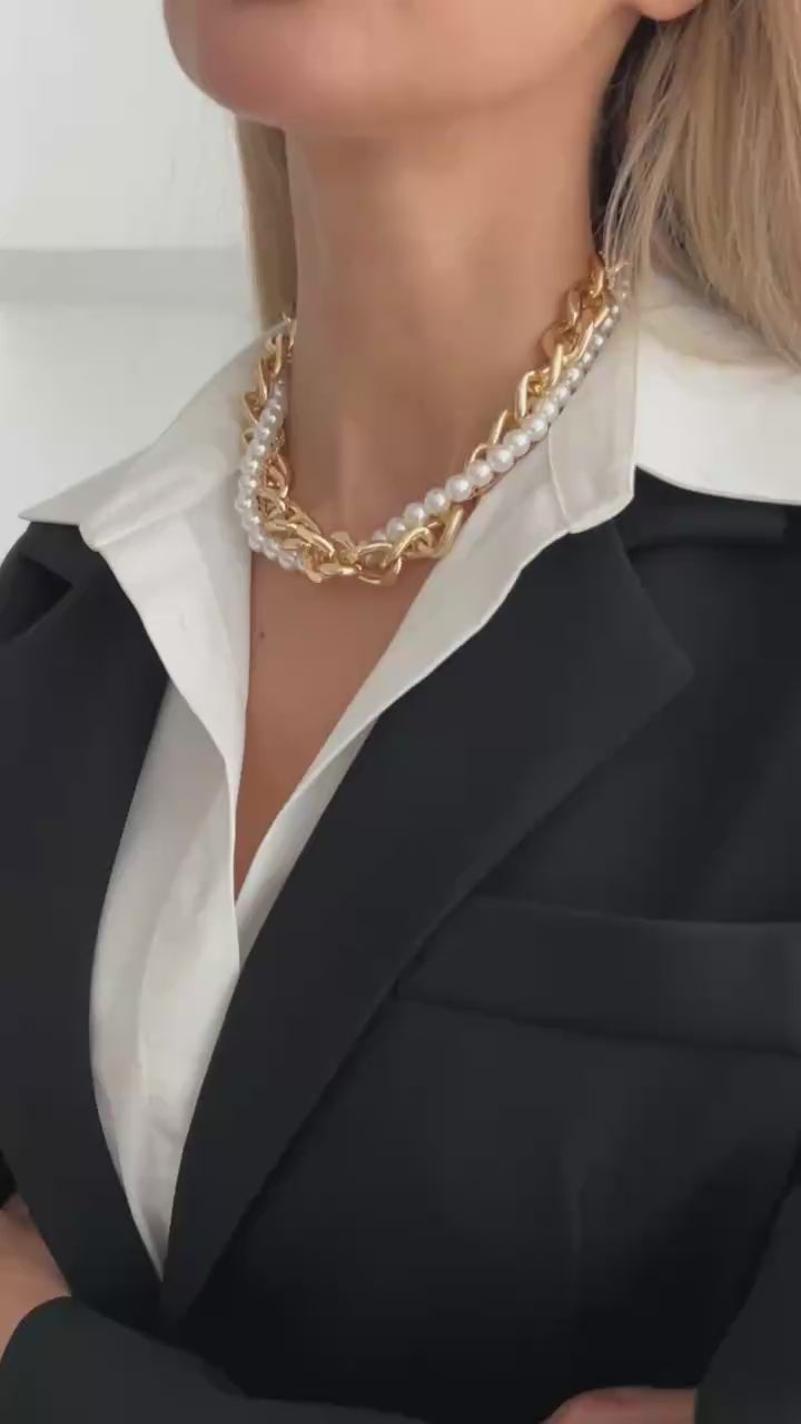 Gold chain and pearl necklace worn by a person with a white jacket.